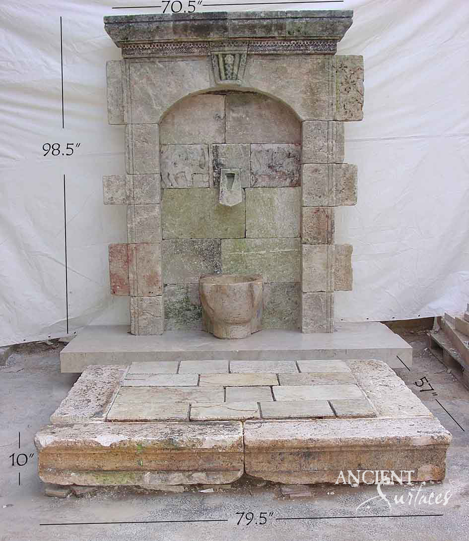 Monumental weathered reclaimed limestone wall fountain with a tall arched niche on a stone base